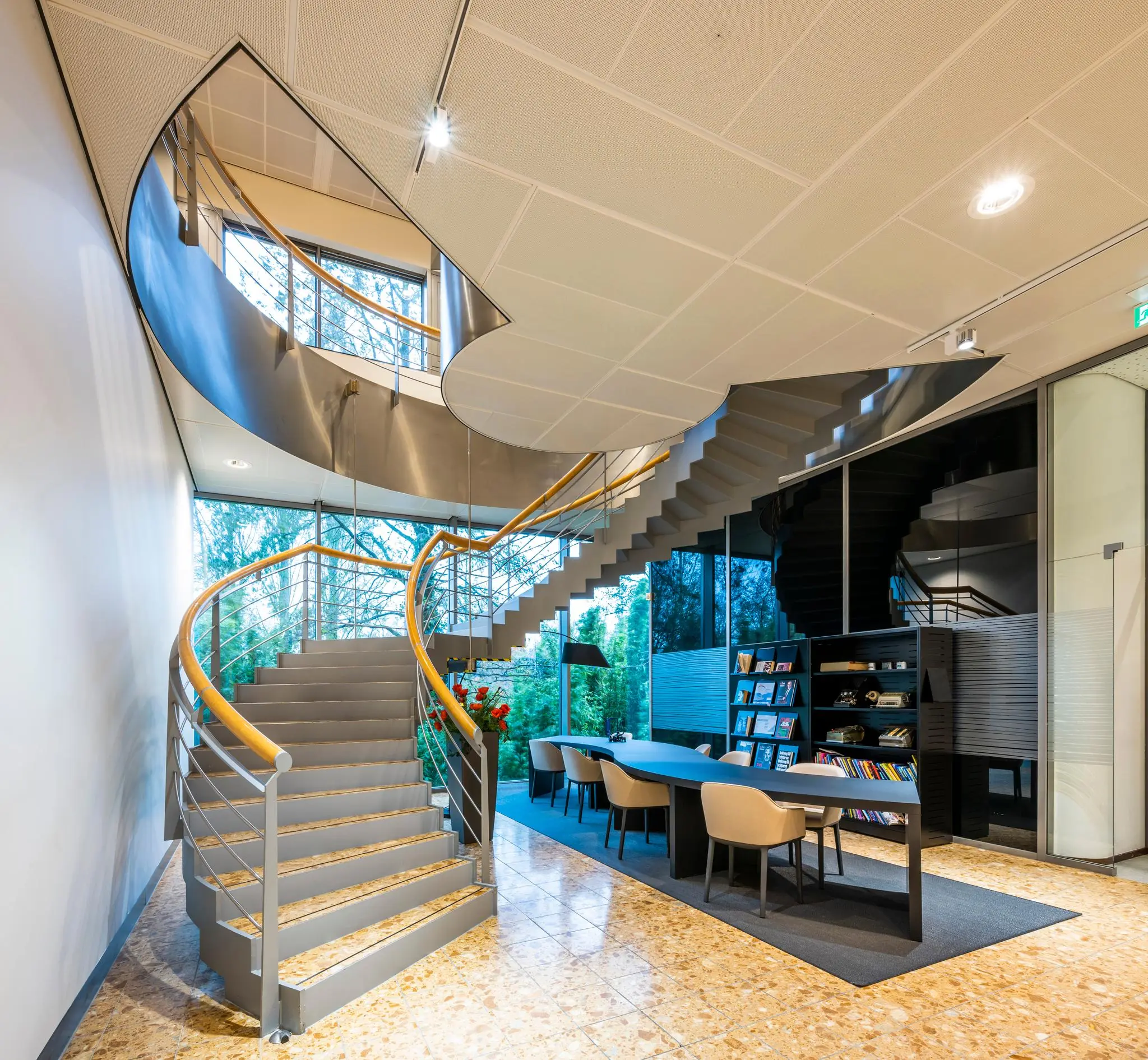 Moderne kantoorruimte aan de Burgemeester Rijnderslaan met een opvallende wenteltrap en een lange vergadertafel naast een tijdschriftenrek.